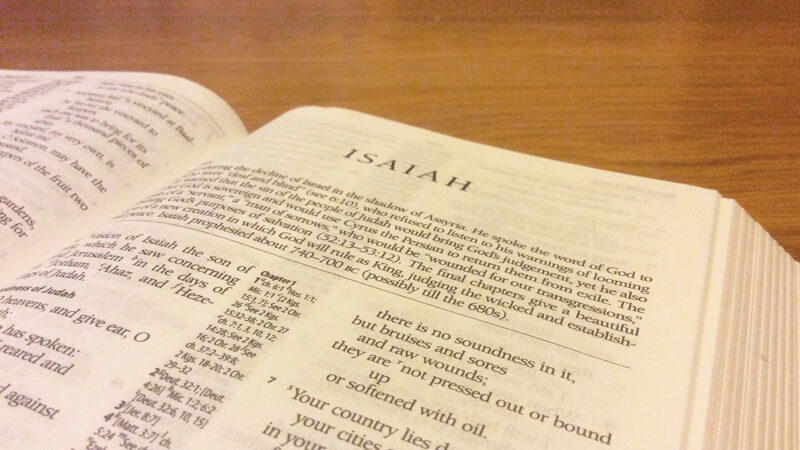 Open Bible on a wooden table displaying the Book of Isaiah with warm lighting.