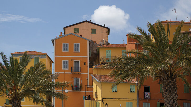 Colorful Mediterranean houses with palm trees under a clear blue sky.