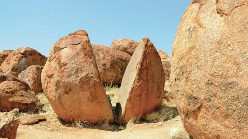 Split boulder at Devils Marbles, Australia, under blue sky, showcasing unique geological formation and natural beauty.