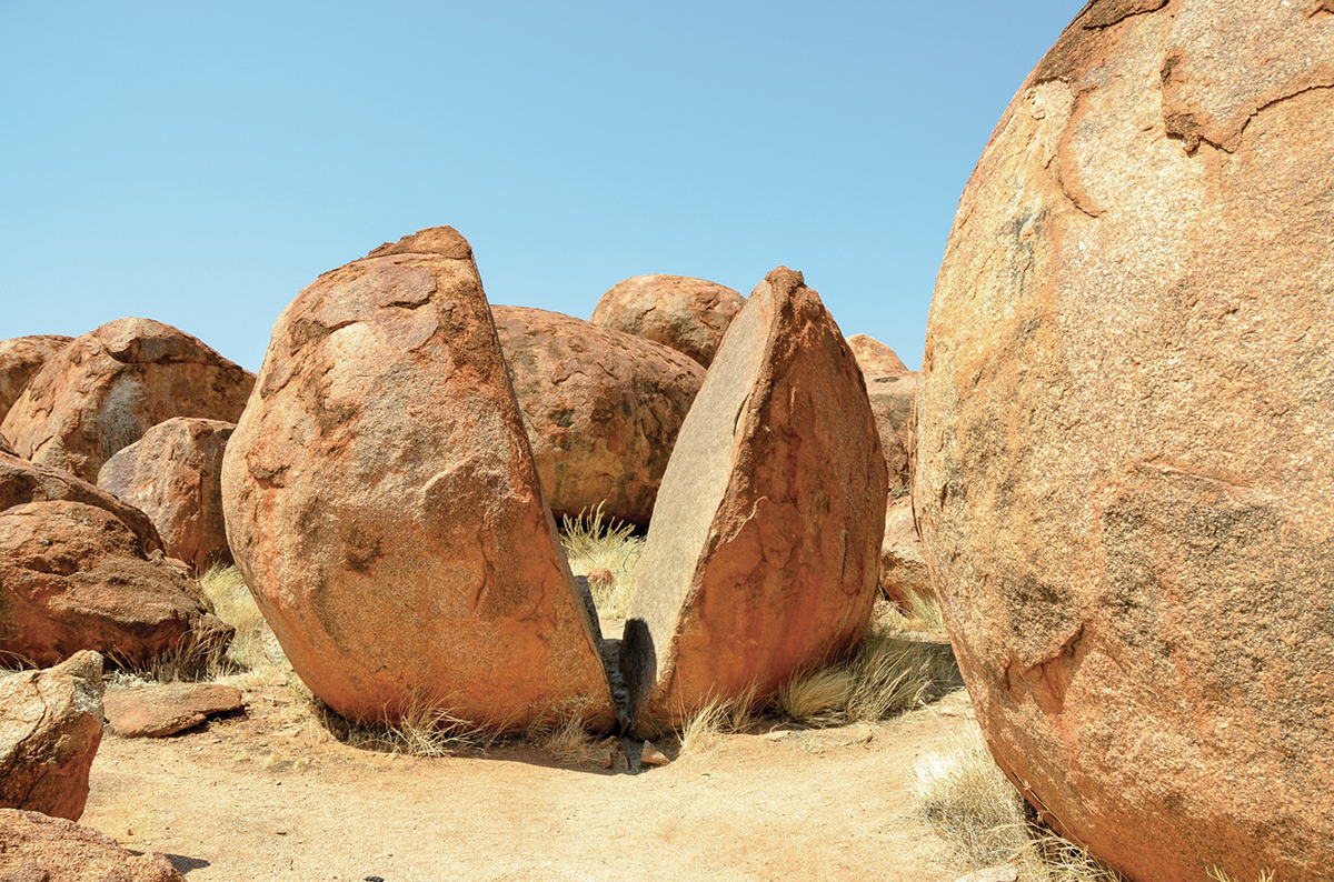 Split boulder at Devils Marbles, Australia, under blue sky, showcasing unique geological formation and natural beauty.