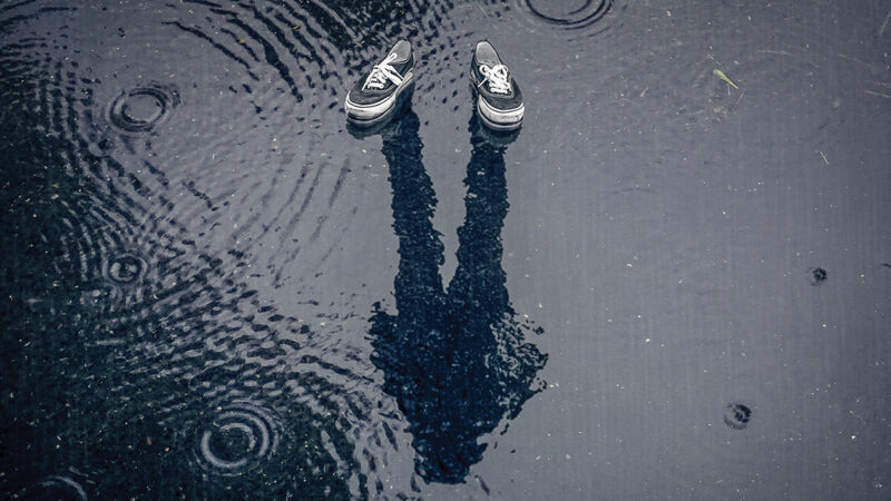 Floating shoes with a human reflection in a rainy puddle, creating an illusion of invisibility.