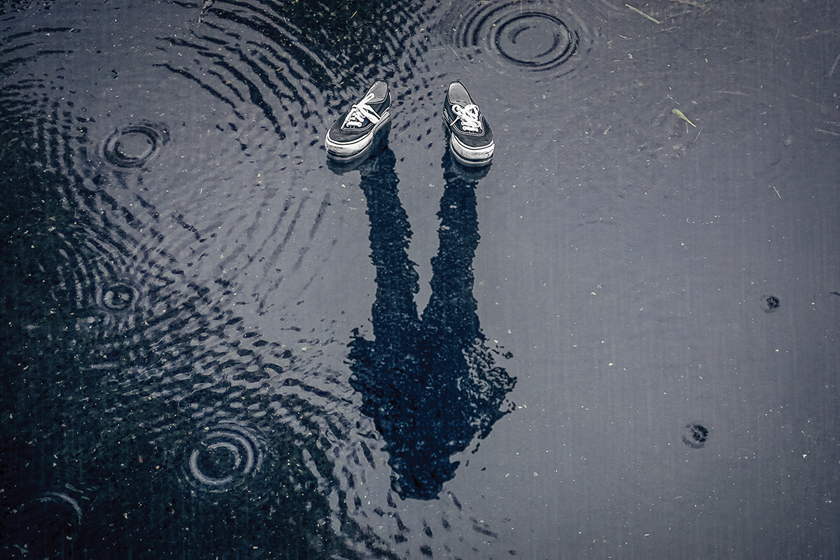 Floating shoes with a human reflection in a rainy puddle, creating an illusion of invisibility.