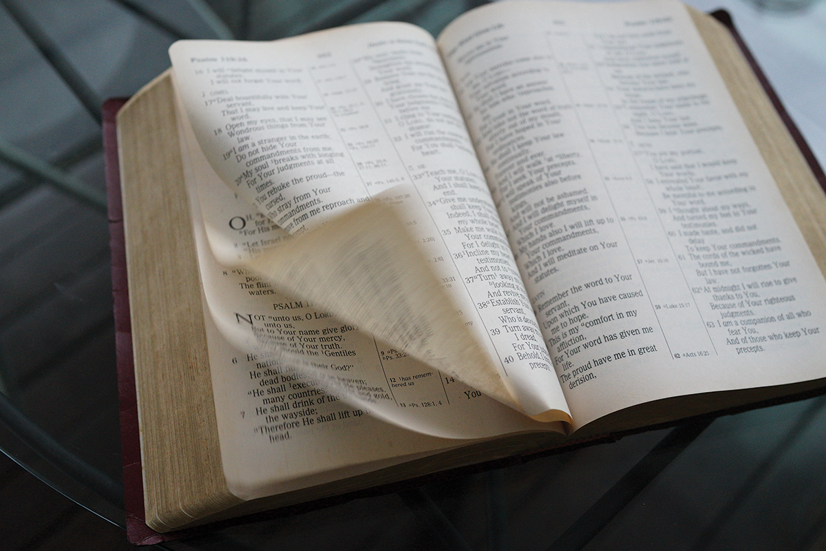 Open Bible with turning pages, showcasing Psalms text, on a glass table.