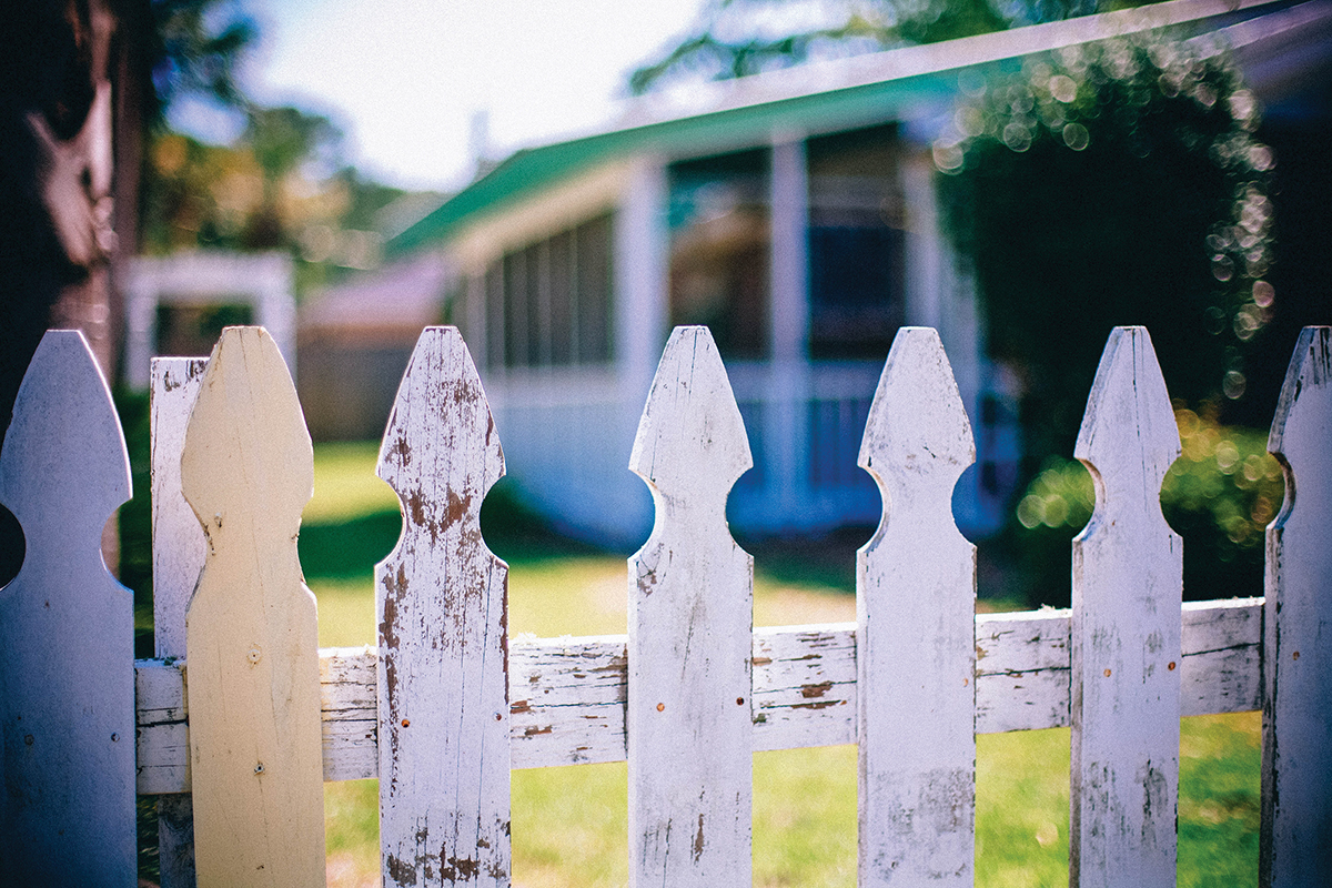 Weathered white picket fence with blurred house background, summer day ambiance.
