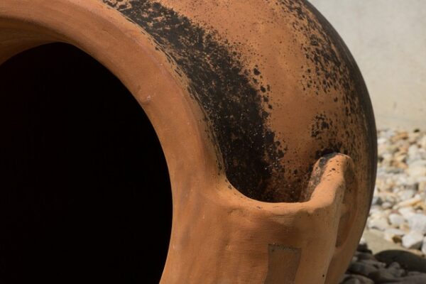 Close-up of a weathered terracotta pot with a handle, showcasing its rustic texture and earthy tones in sunlight.
