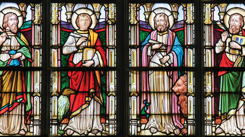Stained glass depicting four religious figures with halos, books, and symbolic animals in vibrant colors.