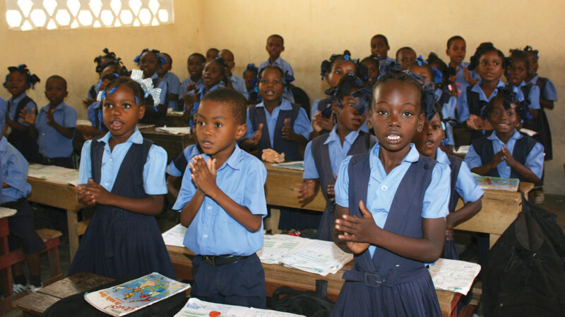 Children in uniform clapping in a classroom, expressing enthusiasm for learning and education.
