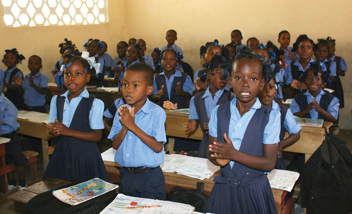 Children in uniform clapping in a classroom, expressing enthusiasm for learning and education.