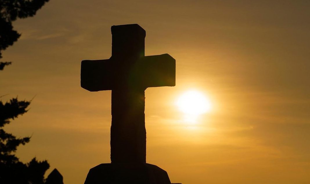 Silhouette of a cross against a vibrant sunset sky, conveying peace and spirituality.