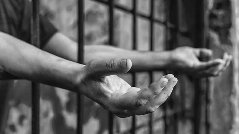 Hands reaching through prison bars, expressing longing and confinement in black and white.