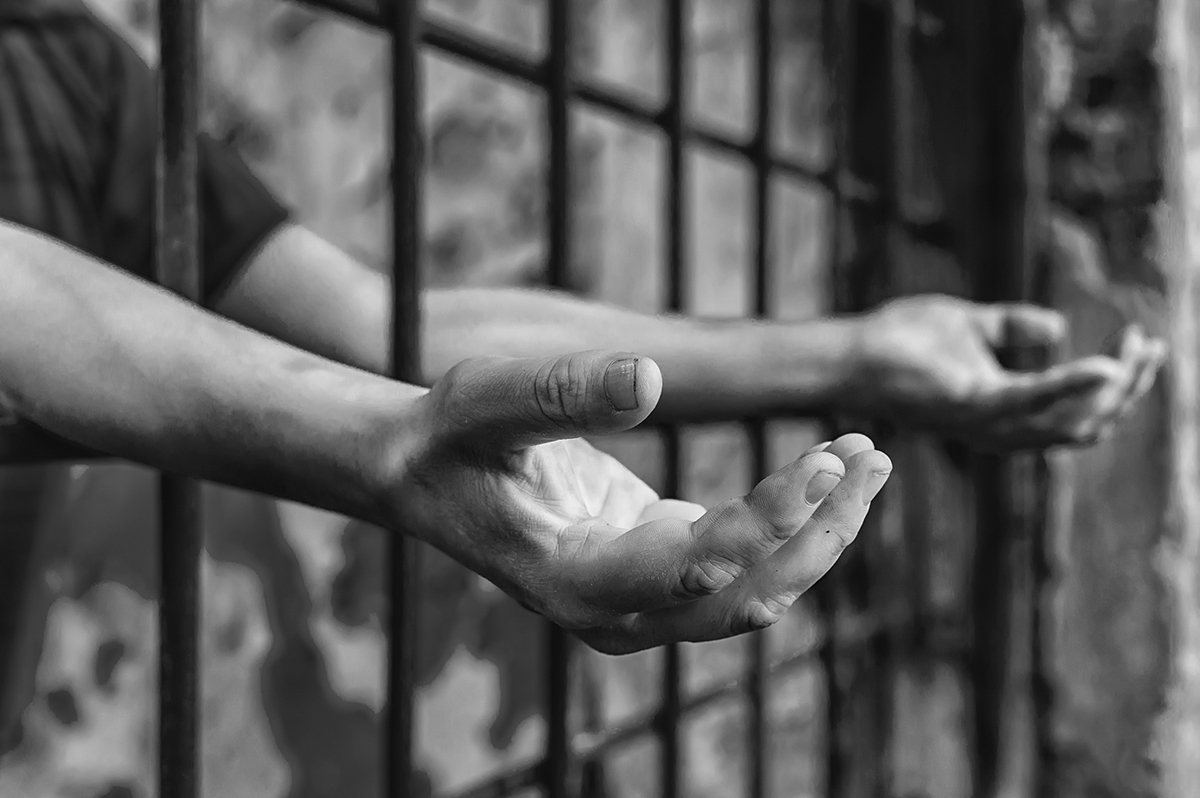 Hands reaching through prison bars, expressing longing and confinement in black and white.