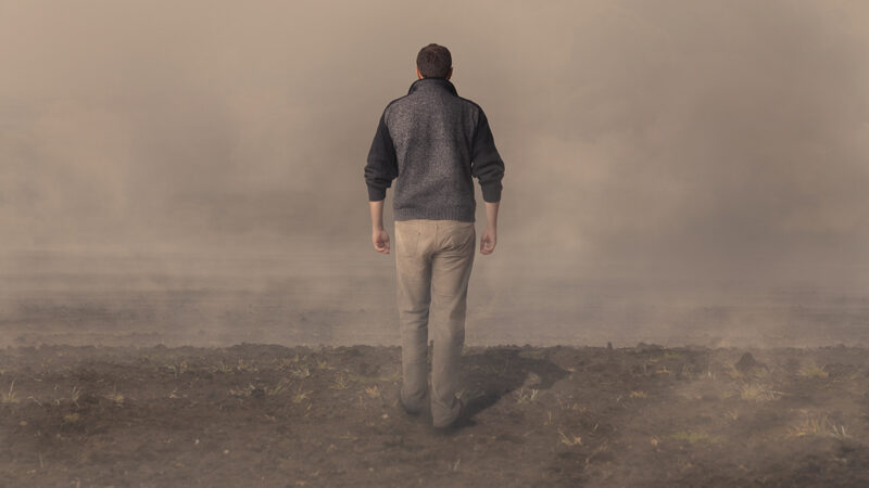 Man walking on barren land into fog, symbolizing uncertainty and solitude.