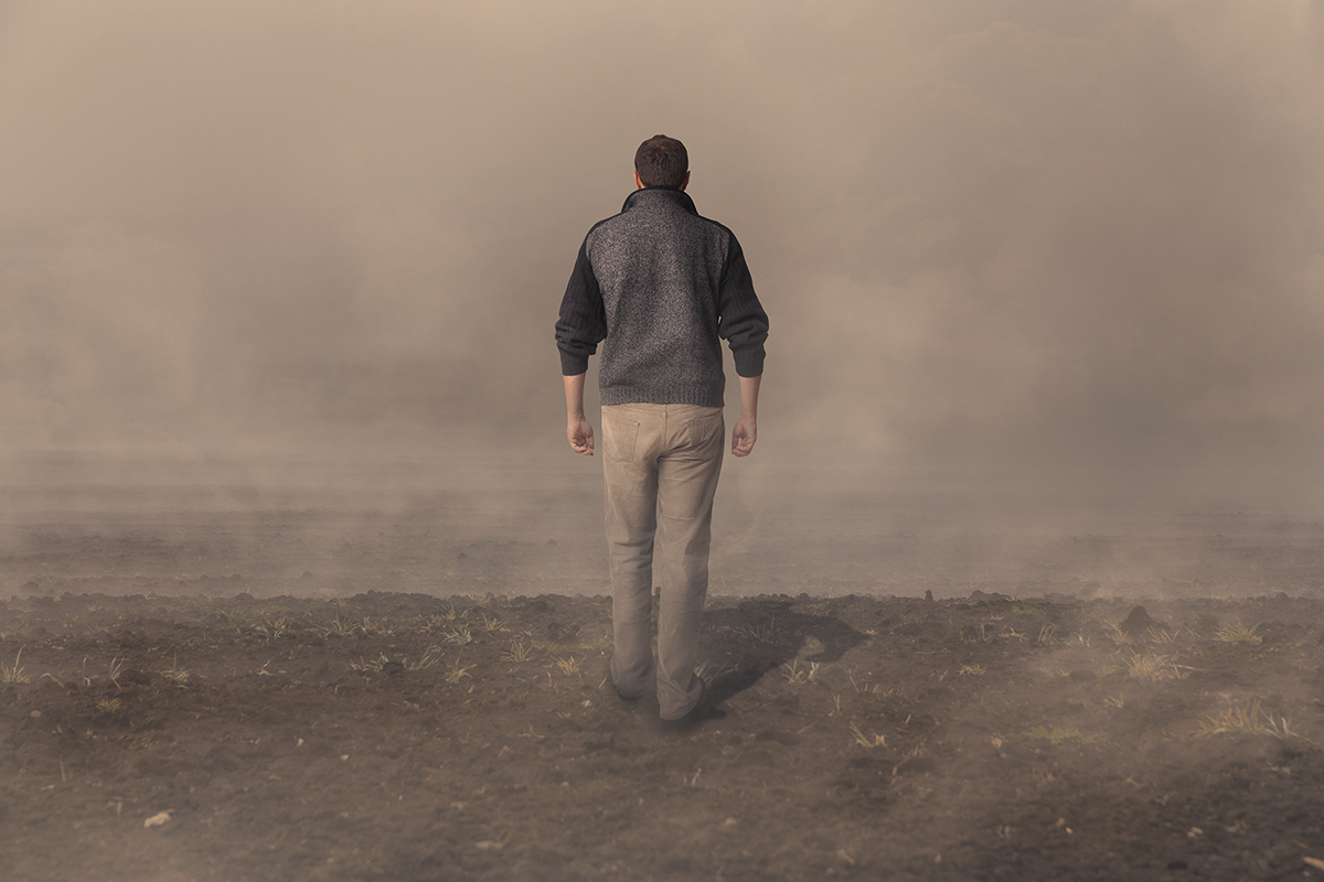 Man walking on barren land into fog, symbolizing uncertainty and solitude.