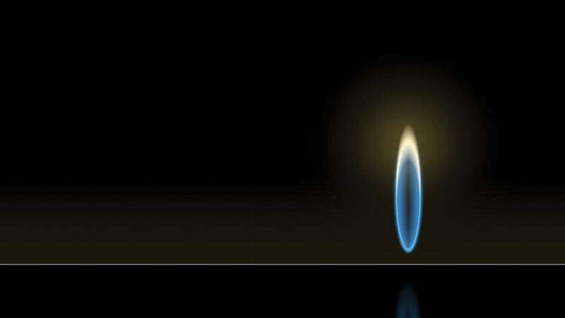 A single blue flame glows against a dark background, casting a soft light and reflection.