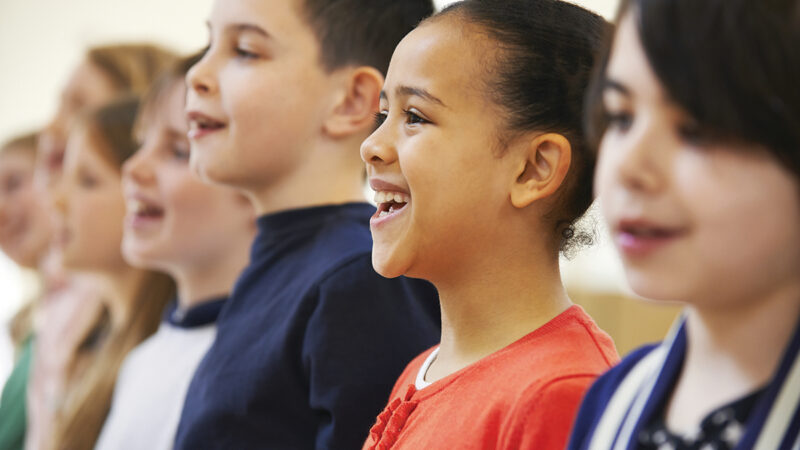 Children singing happily in a choir, showcasing diverse expressions and joy in a classroom setting.