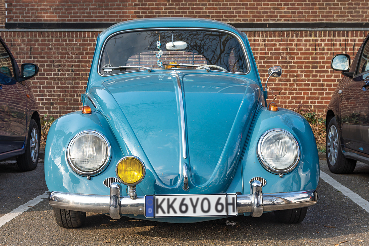 Vintage blue car parked in a lot, front view with distinctive round headlights.