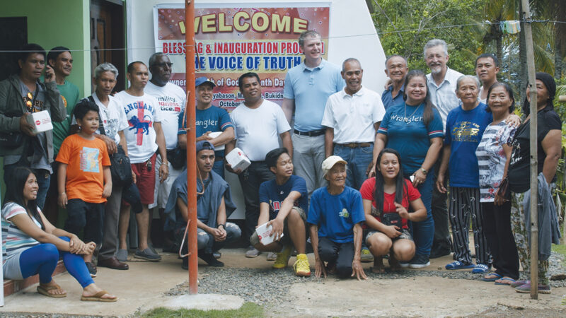 Group photo at community event with Welcome sign, outdoors, smiling people.