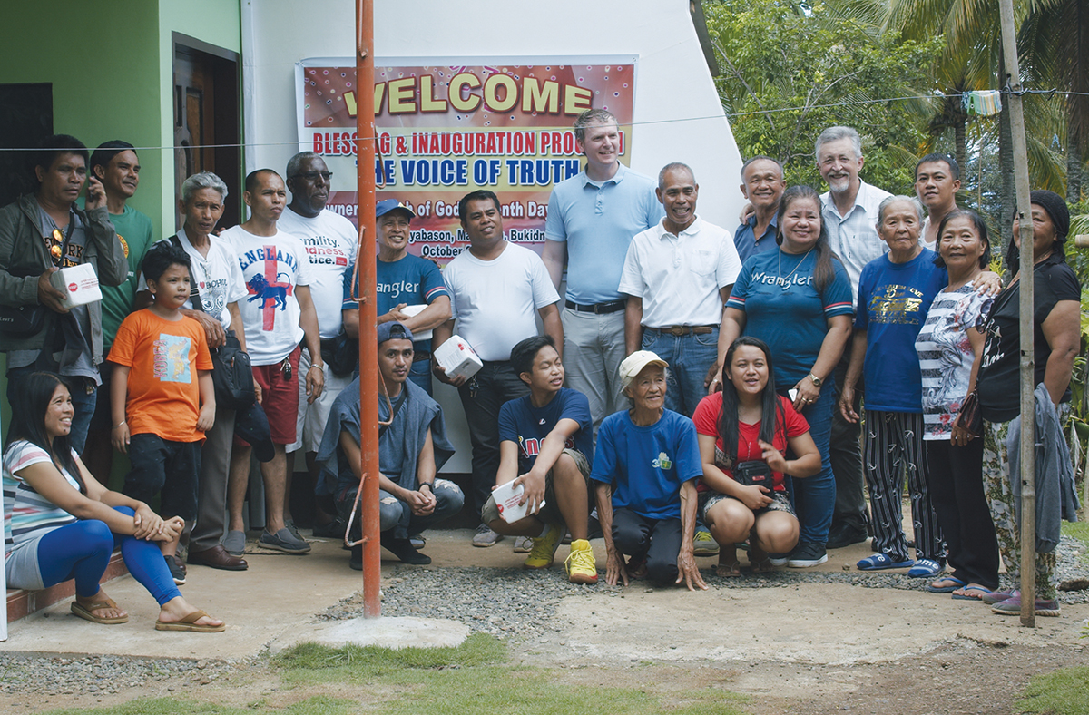 Group photo at community event with Welcome sign, outdoors, smiling people.