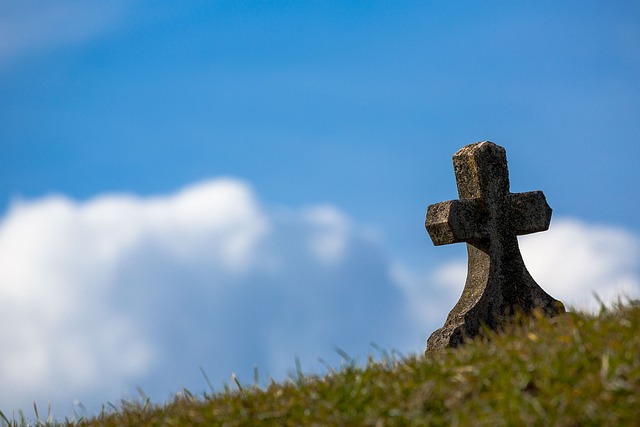 Stone cross on grassy hill against blue sky with clouds, symbolizing peace and spirituality.