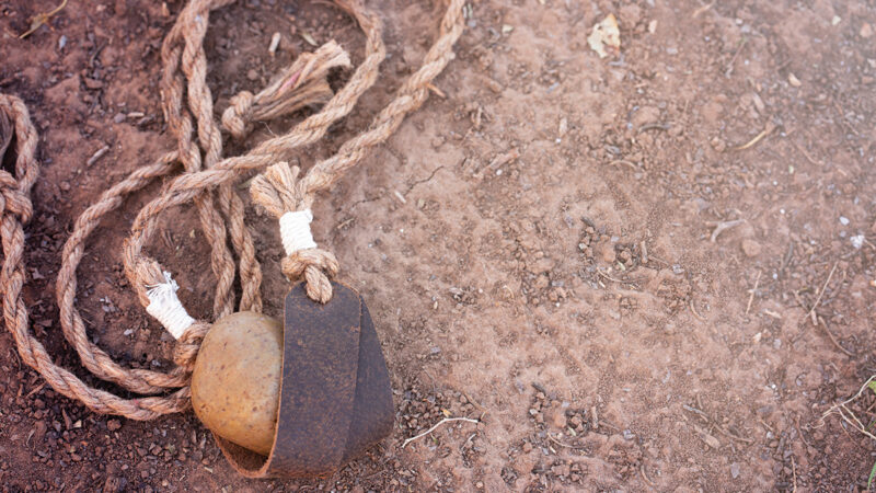 Rope with stone and leather tie on sandy ground, representing traditional tools or crafting elements.