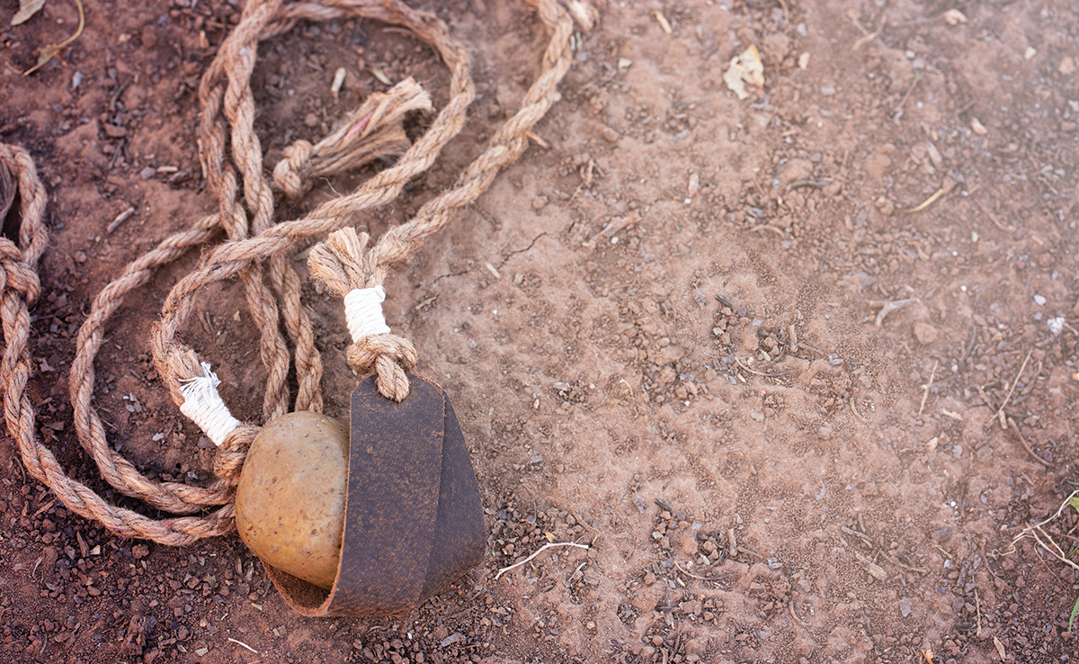 Rope with stone and leather tie on sandy ground, representing traditional tools or crafting elements.