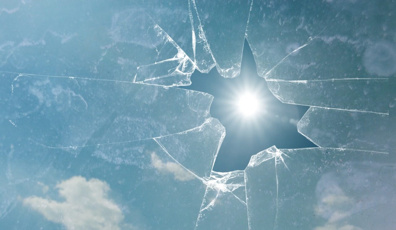 Cracked glass with sunlight shining through against a blue sky backdrop.