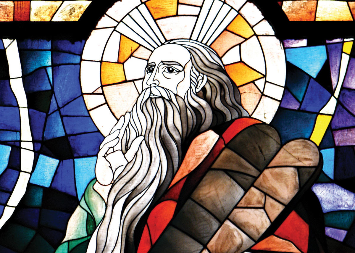 Stained glass depicting a biblical figure with halo, long beard, and colorful geometric patterns in the background.