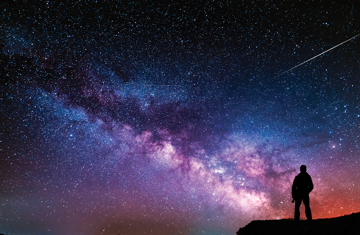 Silhouetted person stargazing under a vivid night sky filled with stars and Milky Way galaxy.