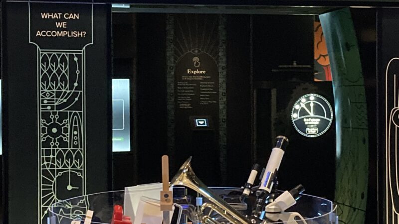 Interactive exhibit with trumpet and telescopes at Our Place display, highlighting human accomplishments in science and art.