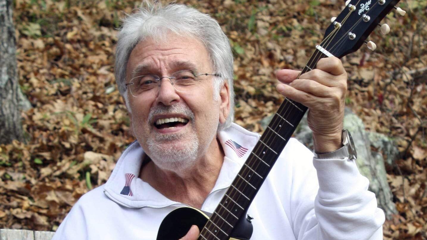 Older man joyfully playing guitar outdoors in autumn setting.