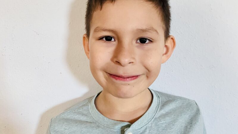 Smiling child in a light blue shirt stands against a white background, capturing a cheerful moment.