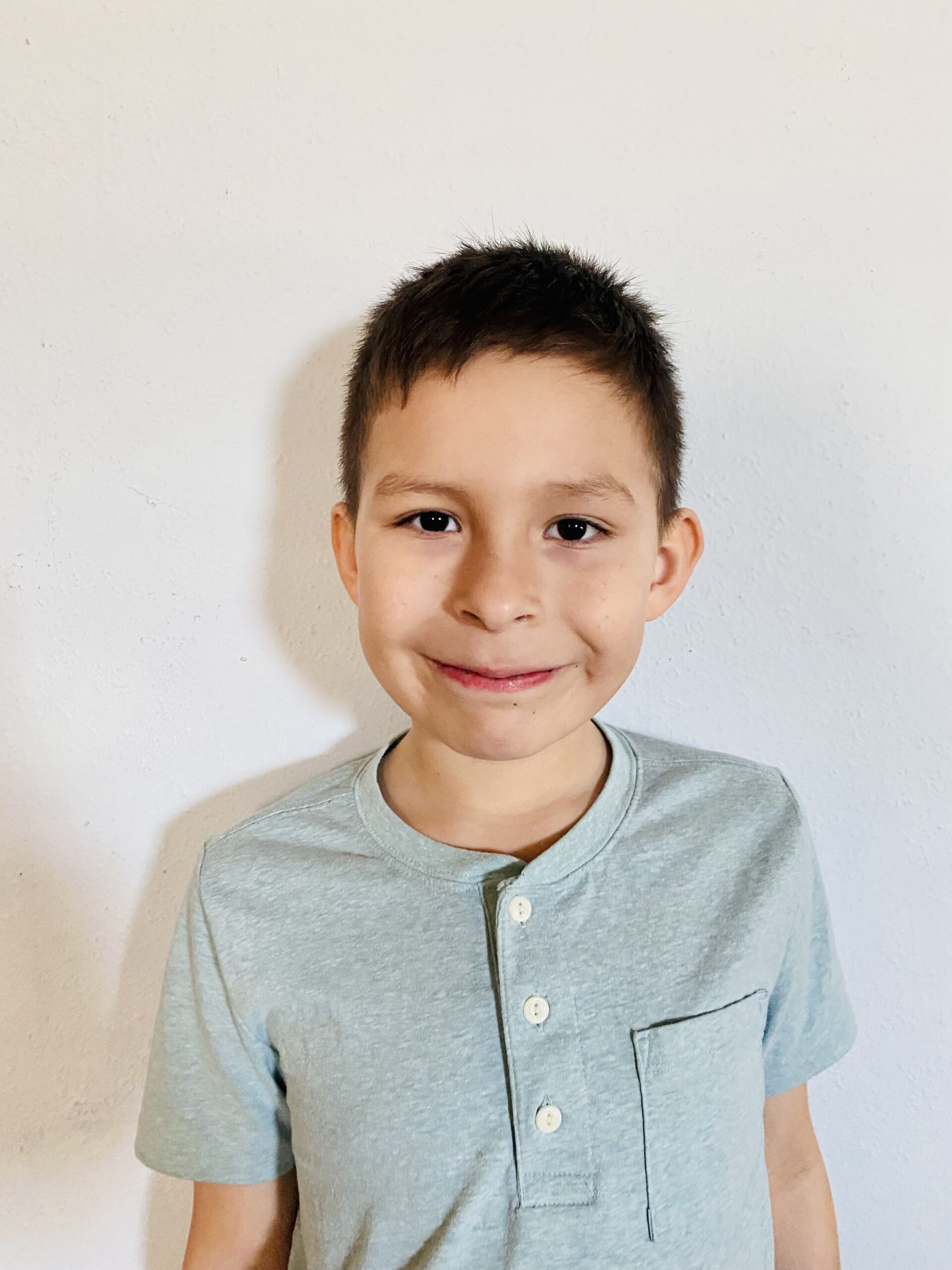 Smiling child in a light blue shirt stands against a white background, capturing a cheerful moment.