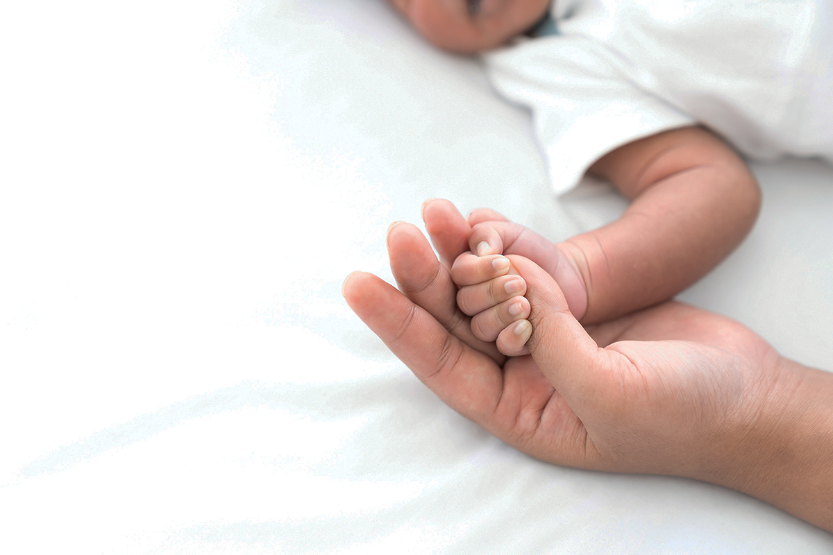 Baby holding parent's hand, symbolizing love and connection. Close-up on soft bedsheet background.