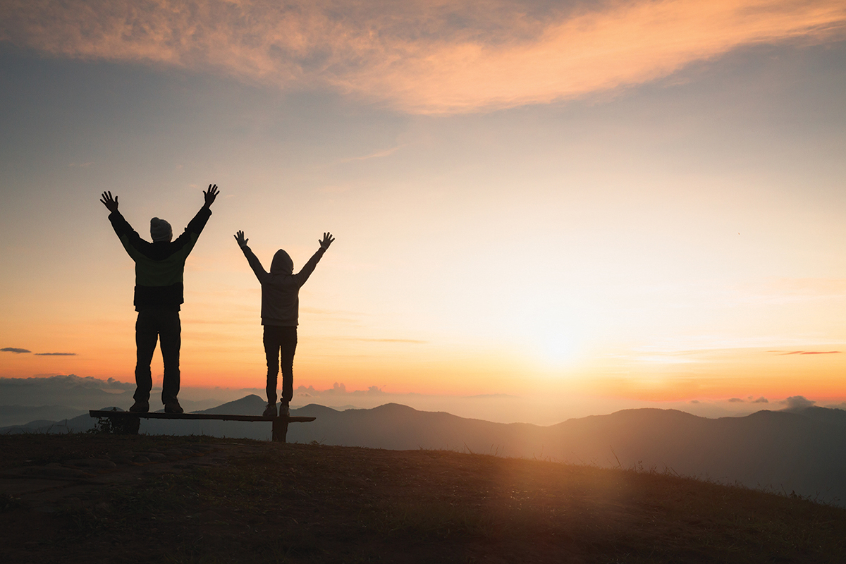Two people celebrating sunrise on a mountain with arms raised, capturing a moment of joy and freedom.