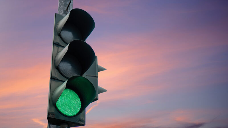 Traffic light showing green under a vibrant sunset sky, signaling to proceed smoothly.
