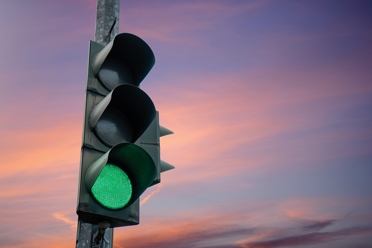Traffic light showing green under a vibrant sunset sky, signaling to proceed smoothly.