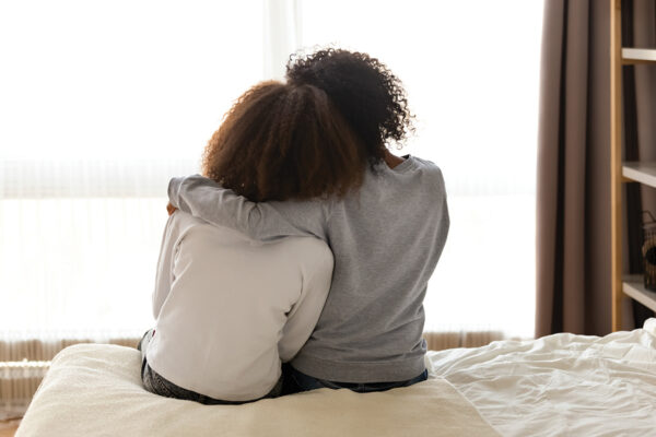 Two people sitting on a bed, embracing with warmth and comfort in a cozy room.