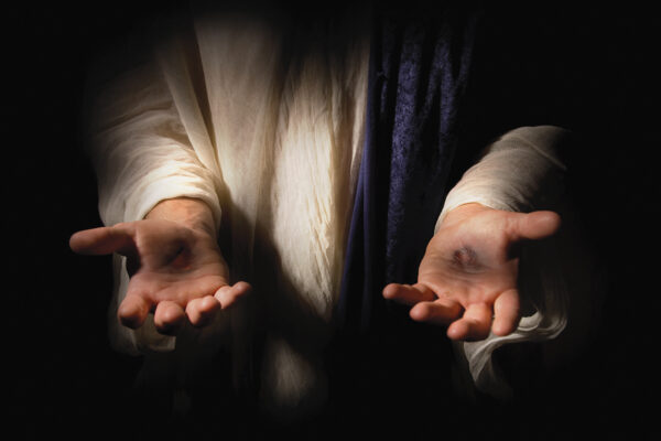 Outstretched hands in dark background, illuminated for emphasis, conveying openness and invitation.