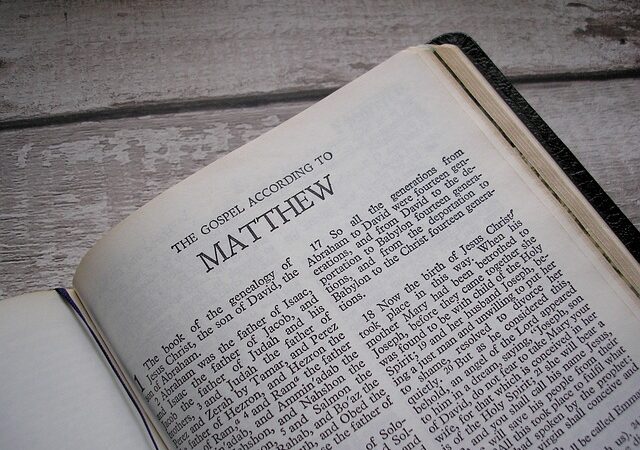 Open Bible displaying the Gospel according to Matthew on a wooden table.