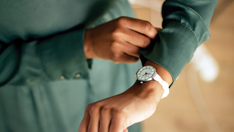 Person adjusting green sleeve while wearing stylish white wristwatch.