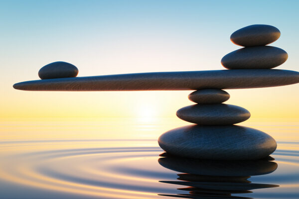 Balanced stones over tranquil water at sunset, symbolizing harmony and stability.