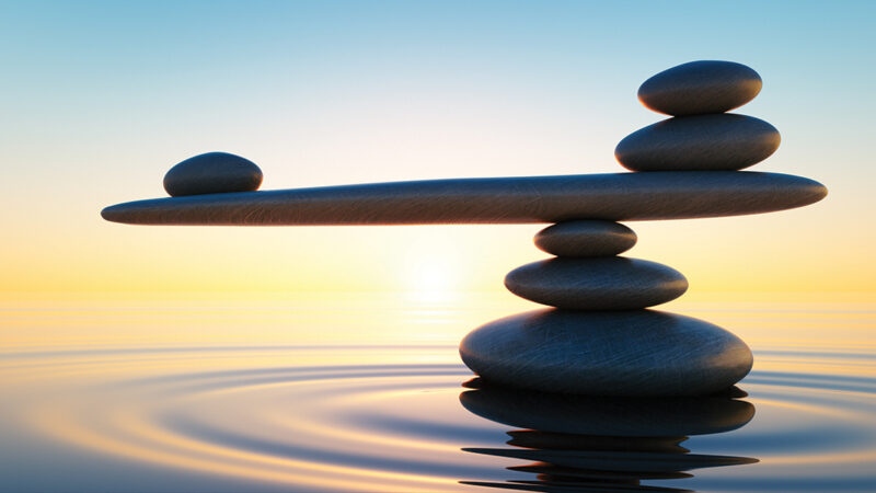 Balanced stones over tranquil water at sunset, symbolizing harmony and stability.