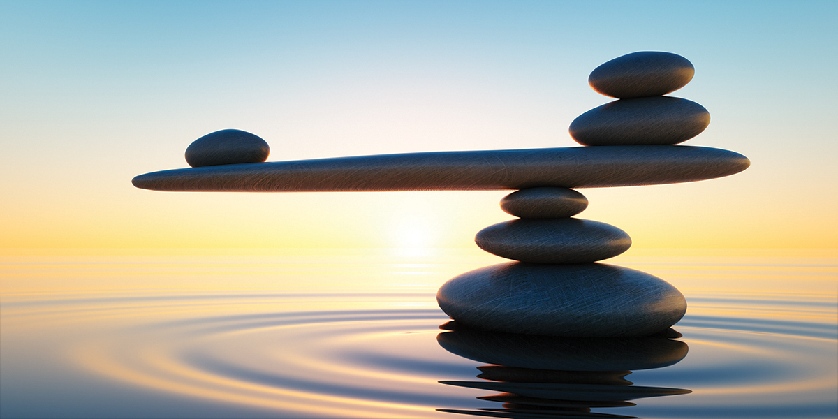 Balanced stones over tranquil water at sunset, symbolizing harmony and stability.