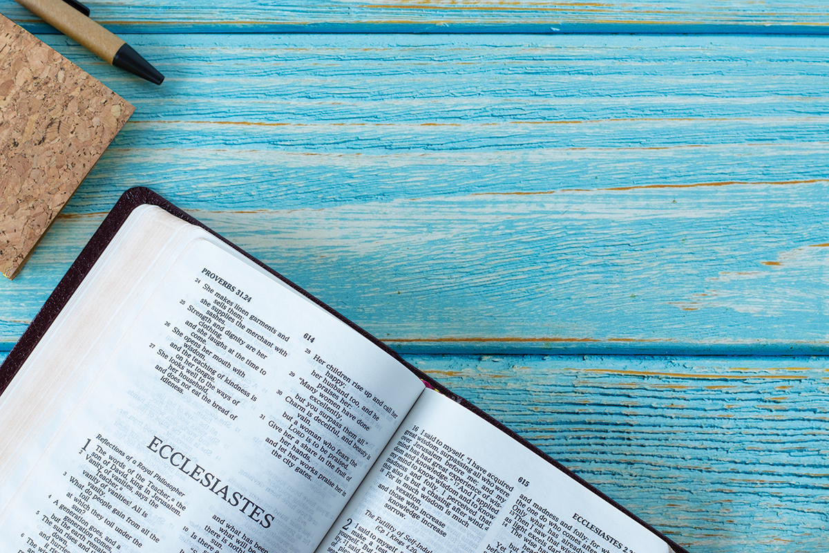 Open Bible on Ecclesiastes with cork notebook and pen on blue wooden background.