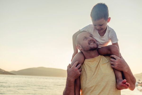 Father and son share a joyful moment by the sea at sunset, embracing happiness and togetherness.