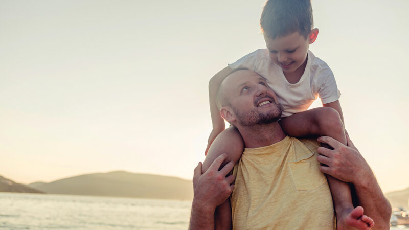 Father and son share a joyful moment by the sea at sunset, embracing happiness and togetherness.