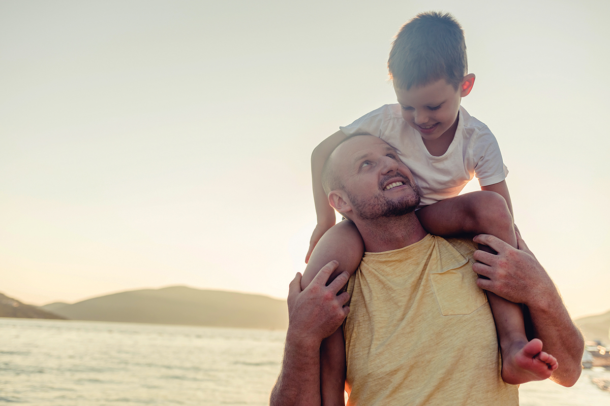 Father and son share a joyful moment by the sea at sunset, embracing happiness and togetherness.