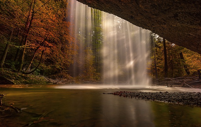 Majestic waterfall cascading in an autumn forest, surrounded by vibrant foliage and serene, reflective waters.
