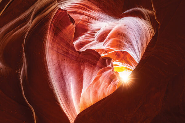Sunlight streams through sandstone curves in Antelope Canyon, highlighting rich reds and textures.