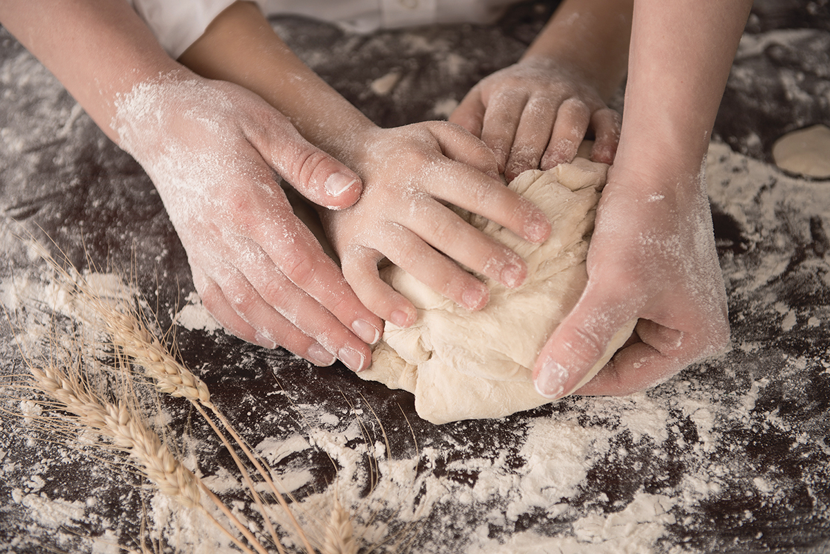 Hands kneading dough on a floured surface, symbolizing baking and family togetherness with wheat stalks nearby.